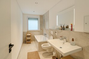 A modern bathroom with a bathtub, toilet, and sink. - Stylish 3-room apartment in Leipzig | Central, modern, and perfect for 6 people (Leipzig)