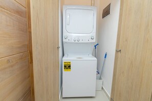 A compact laundry room with a washing machine and dryer, wooden doors, and a mop leaning against the wall.