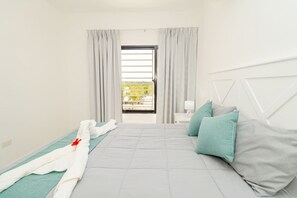 A hotel room with a bed, pillows, a nightstand, and a view of greenery outside. - Tranquil 2BR Sunshine Bayahibe · Pool · Beach 5 min · AC (San Rafael del Yuma)