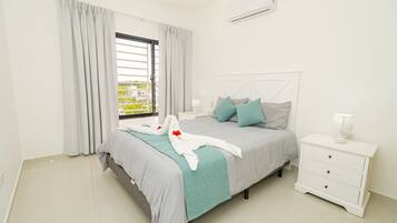 A bedroom with a bed, a nightstand, a lamp, and an air conditioning unit.