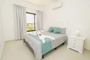 A bedroom with a bed, a nightstand, a lamp, and an air conditioning unit. - Tranquil 2BR Sunshine Bayahibe · Pool · Beach 5 min · AC (San Rafael del Yuma)