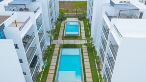A modern hotel with two rectangular swimming pools surrounded by a well-maintained lawn and pathways. - Spacious 3BD Penthouse Private Rooftop Sea Breeze (San Rafael del Yuma)
