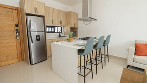 A modern kitchen with a central island, stainless steel refrigerator, wooden cabinets, and a gas stove. - Spacious 3BD Penthouse Private Rooftop Sea Breeze (San Rafael del Yuma)