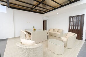 Uma sala de estar espaçosa com uma mesa de vidro, móveis de vime e teto de madeira.