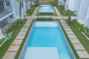 Un hôtel moderne doté de deux piscines rectangulaires, entourées de pelouses bien entretenues et de palmiers.