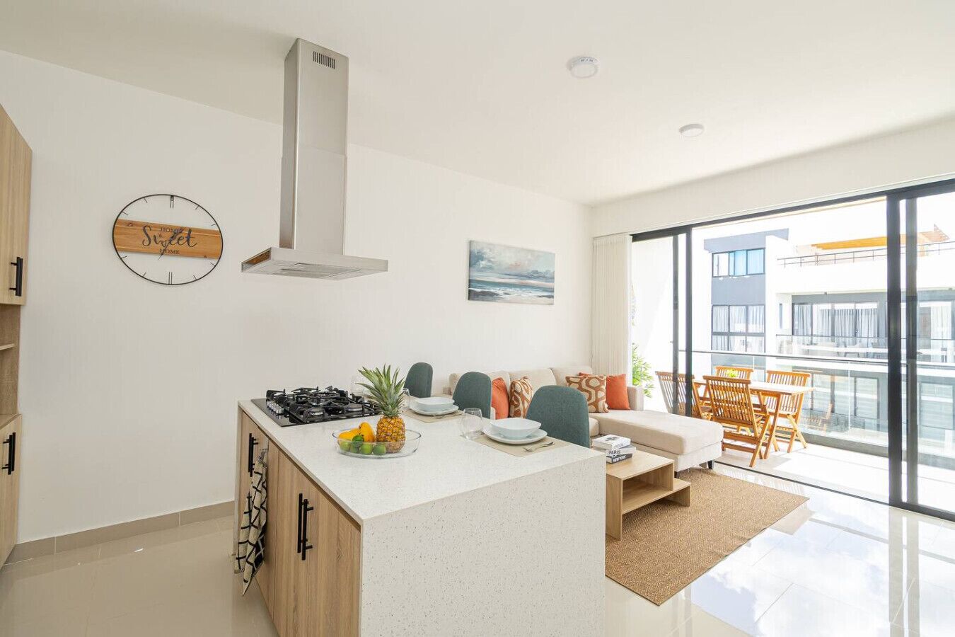 A modern kitchen with a central island, a dining area with a sofa and chairs, and a large window offering a view of the city.