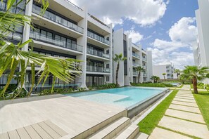 Un hôtel moderne à plusieurs étages, doté d’une piscine, d’un espace extérieur aménagé et de palmiers.