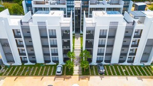 A modern apartment building with a central courtyard, multiple balconies, and a parking area with cars. - Spacious 3BD Penthouse Private Rooftop Sea Breeze (San Rafael del Yuma)