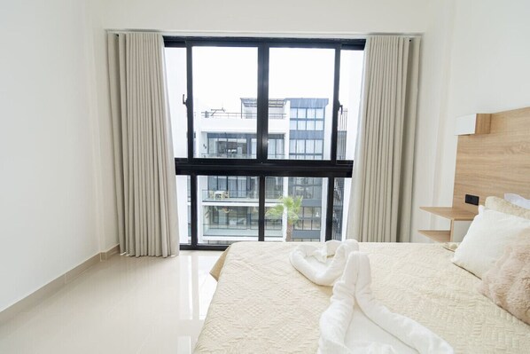 Une chambre d’hôtel avec une grande fenêtre, un lit avec du linge de lit blanc et une tête de lit en bois.
