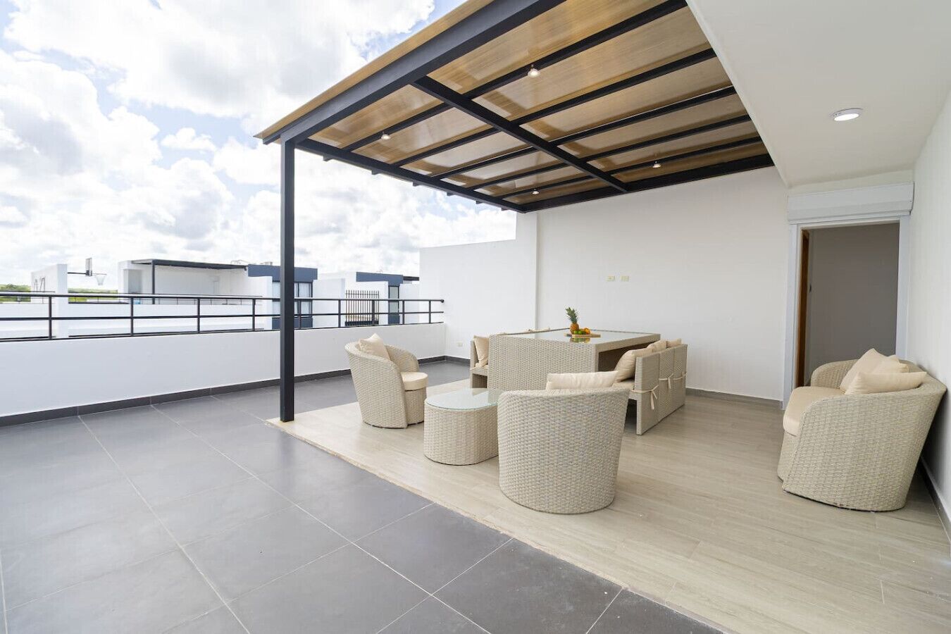 Un área de estar moderna al aire libre con mobiliario de mimbre y una mesa con cubierta de vidrio, que ofrece vistas del horizonte urbano.
