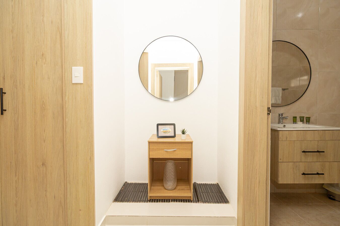 Une salle de bain avec un meuble-lavabo en bois, un miroir rond, un petit tableau encadré et une plante en pot.