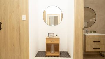 Une salle de bain avec un meuble-lavabo en bois, un miroir rond, un petit tableau encadré et une plante en pot.