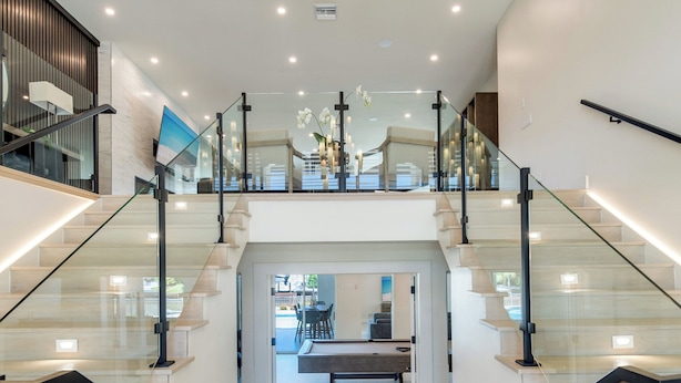 A modern staircase with glass railings and wooden steps, leading to an upper level with a dining area. - Naples Waterfront 3 Master en-suites Pool Boat lift (Naples)