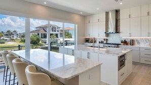 A modern kitchen with a large island, white cabinetry, and a view of a residential area. - Naples Waterfront 3 Master en-suites Pool Boat lift (Naples)