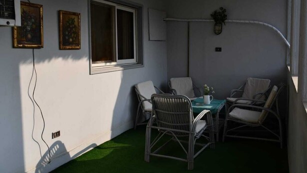 A small, enclosed patio area with wicker furniture, a table, and two windows. - AL Mansour Mohammed, very sunny،Amazing terrace (Zamalek)