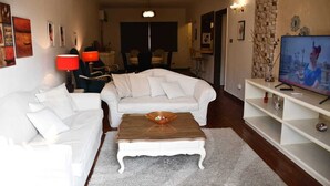 Un soggiorno con un divano bianco, un tavolino in legno e un televisore su un mobile bianco.