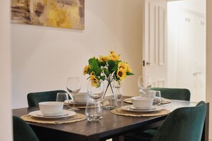 A dining table set with white bowls, wine glasses, and a vase with yellow flowers. - Refined 2-BD Hidden Gem Near Hyde Park (London)