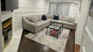 Un salon moderne avec un canapé d’angle, une table basse en verre et une cheminée.