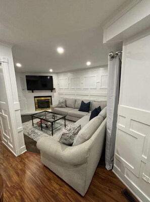 Uma sala de estar com sofá, mesa de centro e televisão de tela plana na parede.