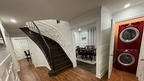 Un escalier mène à une salle à manger où l’on peut apercevoir un lave-linge rouge.