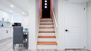 A staircase leading to a door, a dining area with a table and chairs, and white cabinetry in a modern interior. - Stylish, Spacious 6-Bedroom Home in the GTA (Whitby)
