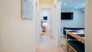 A modern interior with a hallway leading to a dining area, a flat-screen TV mounted on the wall, and a staircase. - Stylish, Spacious 6-Bedroom Home in the GTA (Whitby)