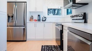 A modern kitchen with white cabinets, stainless steel appliances, and a window with a view of trees. - Stylish, Spacious 6-Bedroom Home in the GTA (Whitby)