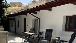 An outdoor patio with a table and chairs, a potted plant, and a window overlooking a residential area. - Monolithos Cottage in the Troodos Mountains above Limassol (Pachna)