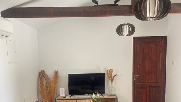 A living room with a brown sofa, a wooden coffee table, a TV on a wooden stand, and a wooden door. - Monolithos Cottage in the Troodos Mountains above Limassol (Pachna)