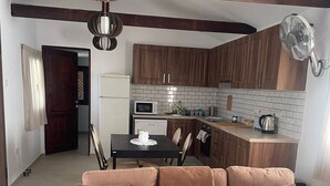A modern living room with a sofa, a coffee table, and a plant. There is a kitchen area with wooden cabinets and a microwave. - Monolithos Cottage in the Troodos Mountains above Limassol (Pachna)
