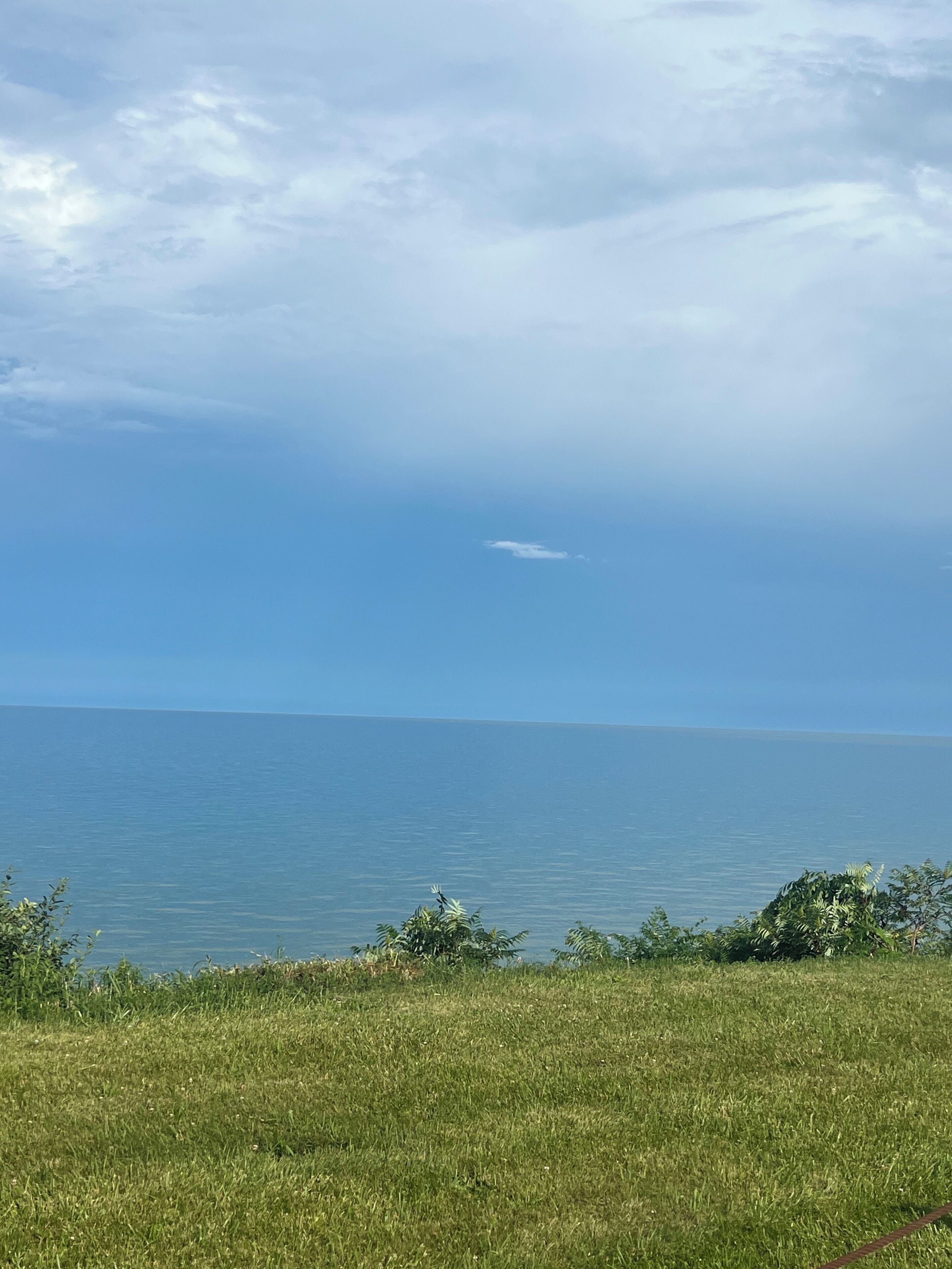 A grassy field with a view of the sea and a partly cloudy sky.