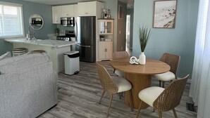 A modern kitchen with white cabinets, stainless steel appliances, and a dining area with a wooden table and wicker chairs. - Longfellow Tides (Lexington)