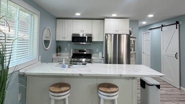 A modern kitchen with white cabinets, stainless steel appliances, and a large island with stools. - Longfellow Tides (Lexington)