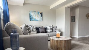 En moderne stue med en grå sofa, et rundt træbord og en blå vase på et sofabord.