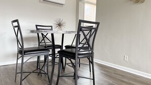 En spiseplads med et marmorbord, fire sorte stole, en dekorativ vægdekoration og en aircondition.