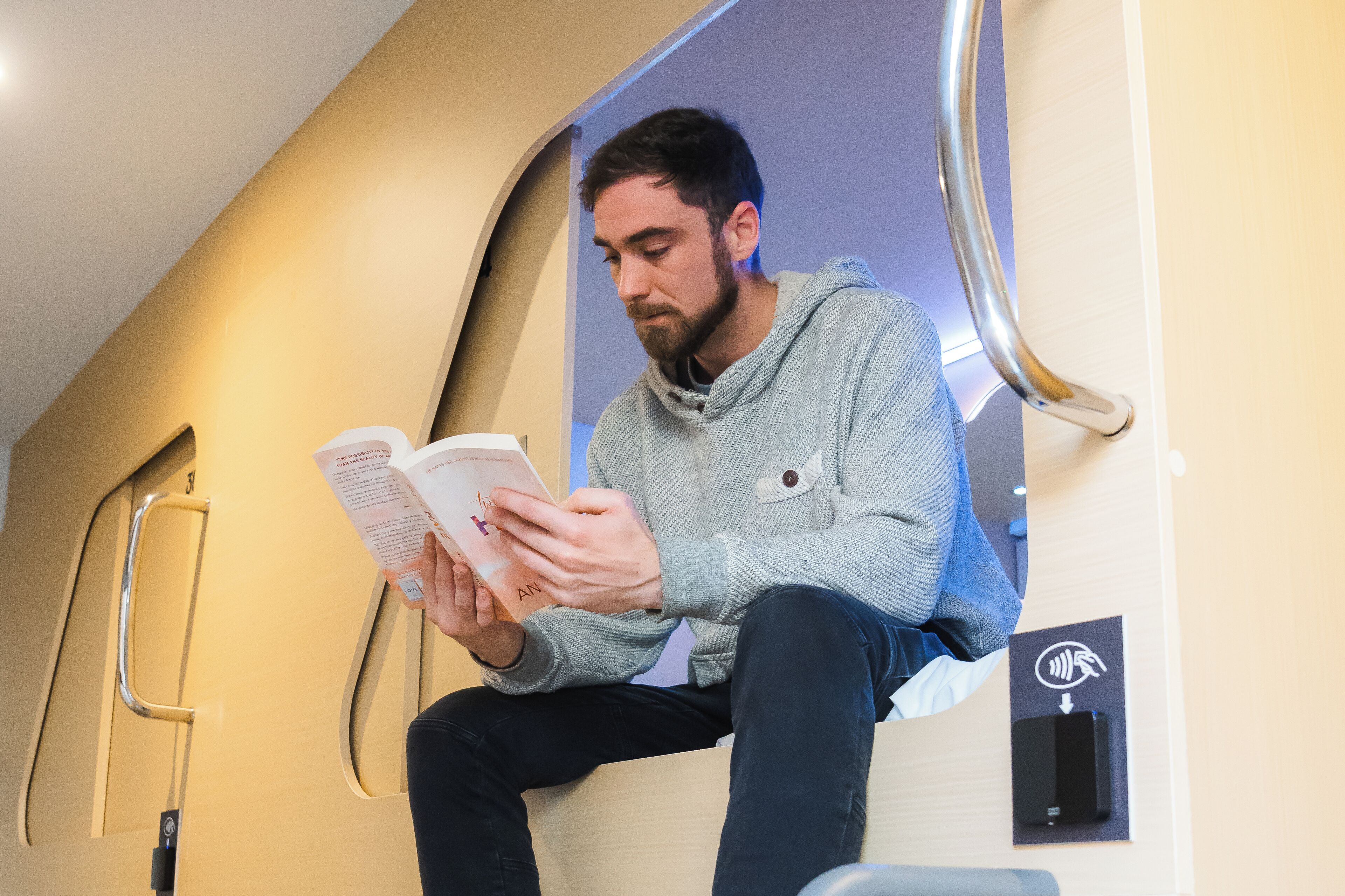 A person sitting on a bench inside a train, reading a book.