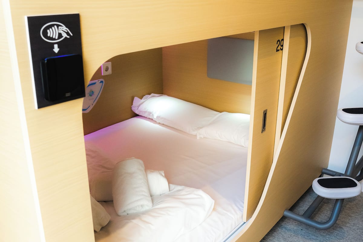A compact, single-bed room with a built-in desk and a small seating area.