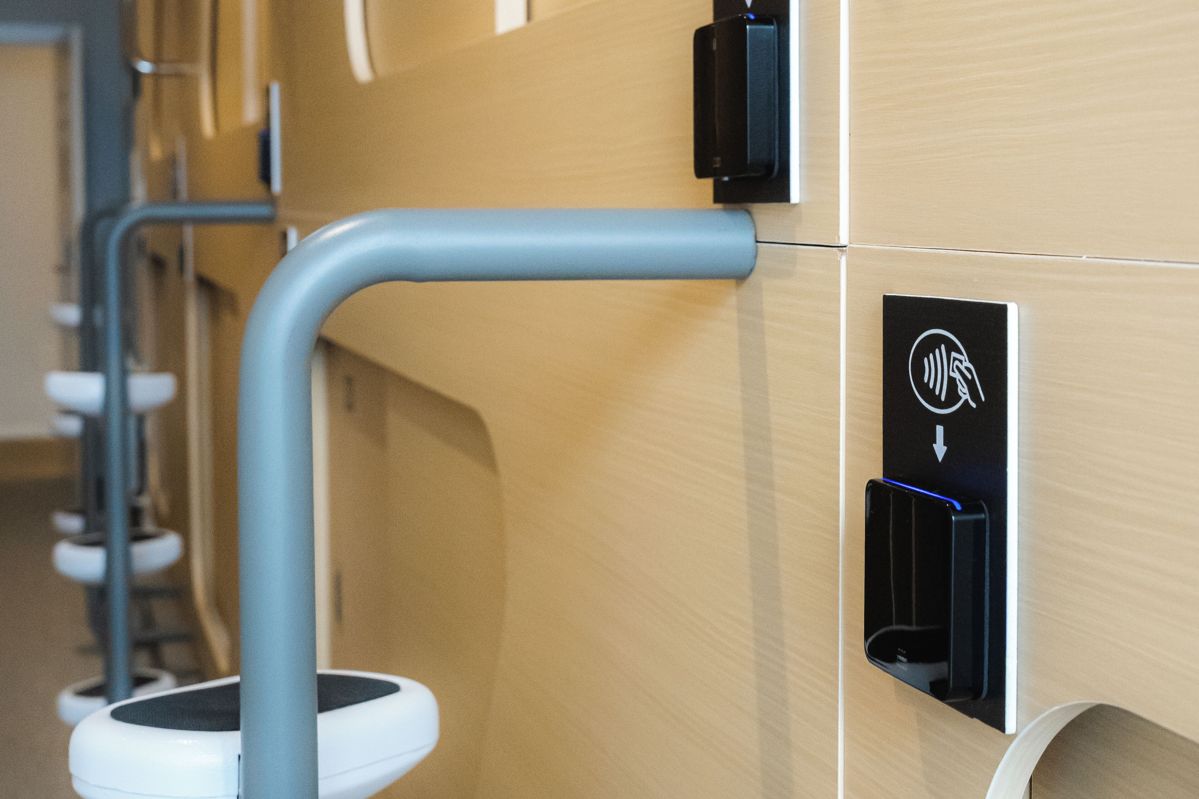 A modern bathroom with a toilet, a hand sanitizer dispenser, and a charging station.