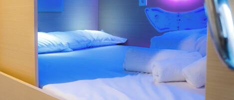 Een moderne hotelkamer met een net opgemaakt bed, een hoofdbord met ingebouwde verlichting en een klein rond spiegel.