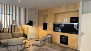 A modern kitchen with wooden cabinets, a black countertop, and a coffee machine. There is a seating area with a sofa and chairs. - Urban Cube Hostel Granada (Granada)