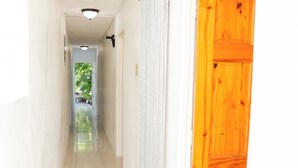 A hallway with a wooden door on the right, white walls, and a tiled floor.