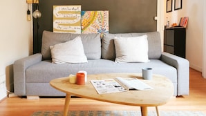 En moderne stue med en grå sofa, to hvide puder, et træbord med en avis, et stearinlys og en kop.