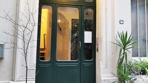 En grøn døråbning med to døre, en lampe over døren, en lille potteplante til venstre og en større potteplante til højre.