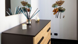 A room with a wooden dresser, a mirror, and wall art depicting flowers and butterflies. - Spacious apartment in central area with balcony, within walking distance of Scassi Hospital (Genova)