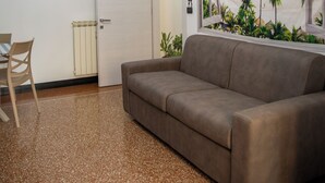 A living room with a brown sofa, a dining table with chairs, a ceiling light fixture, and a beach mural on the wall. - Spacious apartment in central area with balcony, within walking distance of Scassi Hospital (Genova)