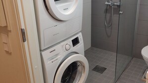 A laundry area with two Samsung washing machines, a glass shower enclosure, and a toilet.