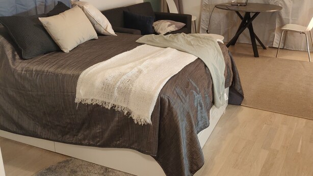A modern bedroom with a large bed, a small table with a laptop, and a chair.