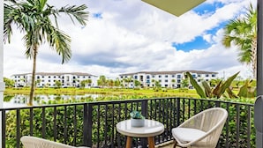 A balcony with wicker chairs, a small round table, and a view of a building across a pond. - Modern 2BR Fort Myers Condo Pool, BBQ & Near Beaches (Fort Myers)