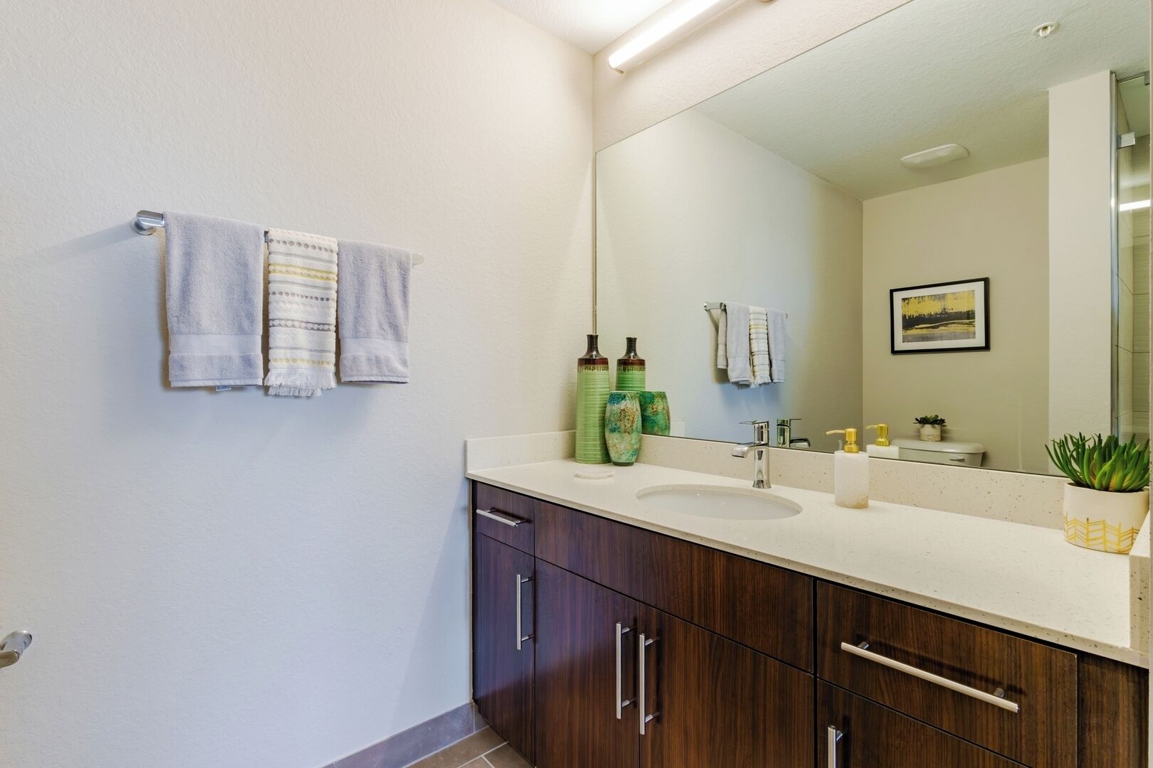 A bathroom with a large mirror, a sink, and two towels hanging on the wall.