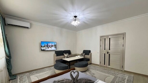 A hotel room with a bed, a chandelier, a television, a sofa, and a dining table.